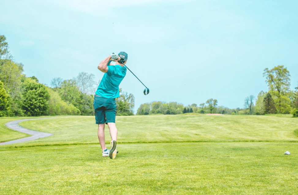 man hitting a long drive on a golf course in a blue shirt