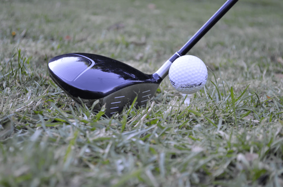 Driver shown with ball on tee in grass up close